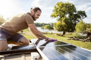 A man is up on the roof of his caravan checking his solar panels during a sunny day