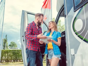 A happy couple are standing at the front door of a new RV in the dealer lot as they weight up features and price so they can get a quick RV loan approval through Jade Caravan Finance